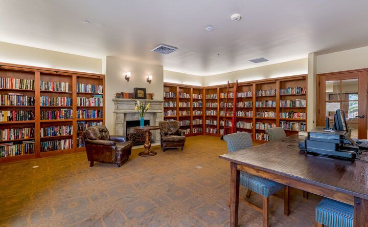 Cozy library reading room with bookshelves, a fireplace, and comfortable seating.