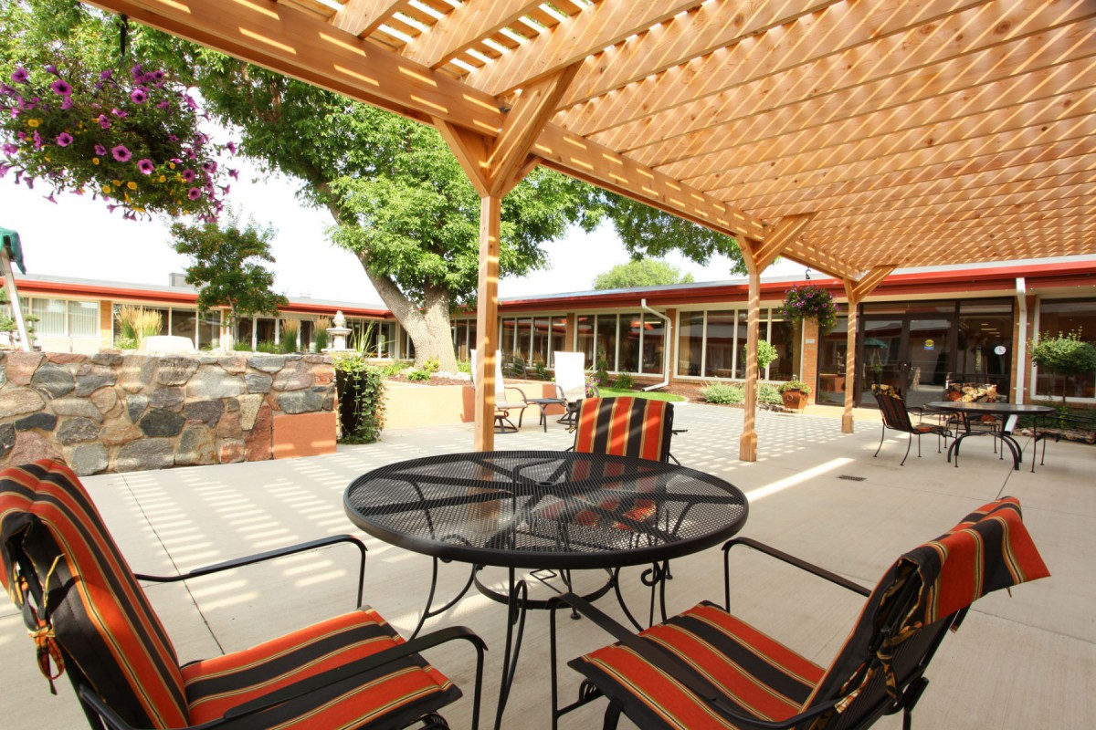 A cozy outdoor patio area with a pergola, featuring a table and chairs set in a sunlit courtyard.
