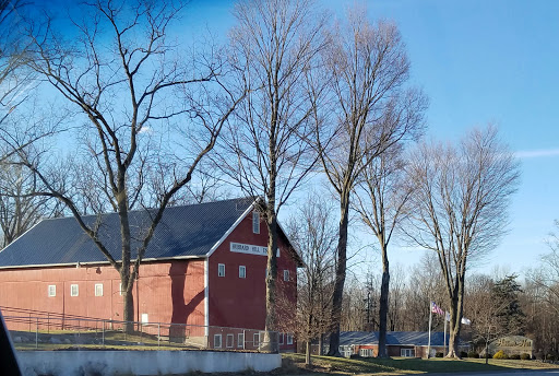 A picturesque red barn surrounded by leafless trees under a clear blue sky.