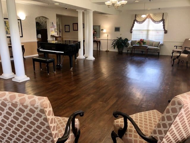 A spacious living room with a grand piano, elegant furniture, and wooden flooring.