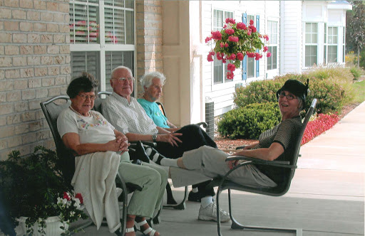 A group of seniors enjoying a sunny day on the porch, engaged in conversation.