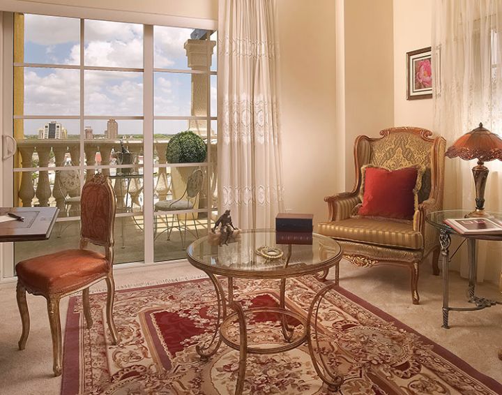 A classic living room with elegant furnishings, featuring a glass table and armchair, overlooking a balcony.