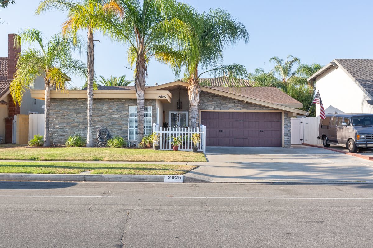 A suburban house with palm trees and a driveway leading to a two-car garage.