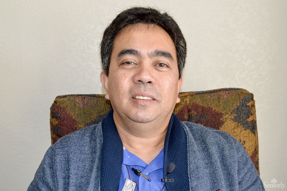 A man in casual clothing sits indoors, looking at the camera.