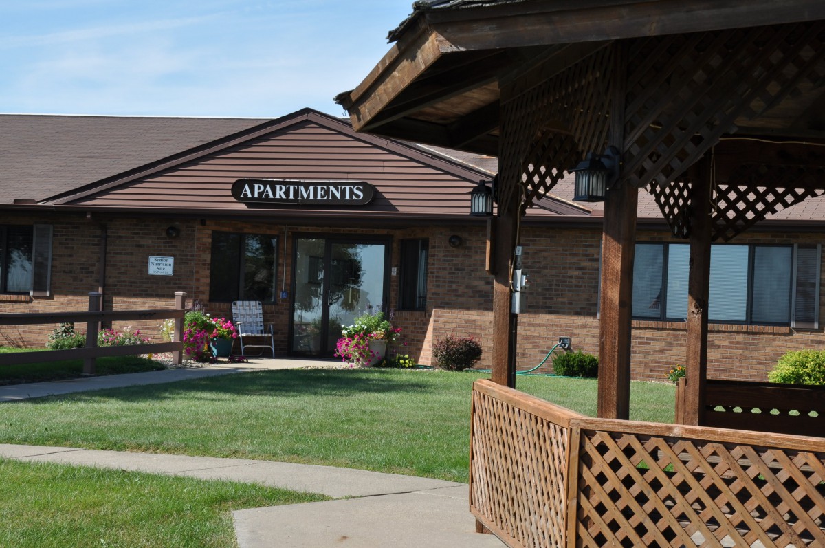 A view of an apartment building entrance with a gazebo and well-kept lawn.