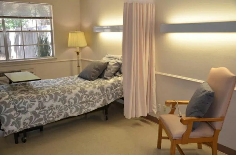 A cozy bedroom with a bed, lamp, chair, and window.