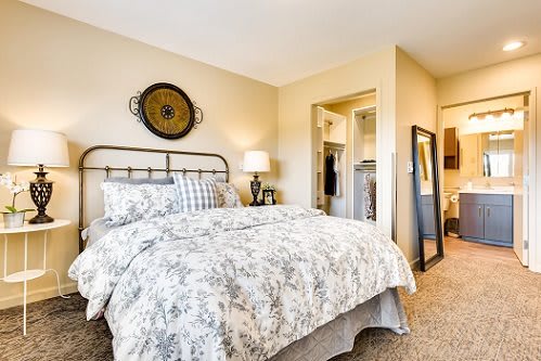 A cozy bedroom with a neatly made bed, decorative wall art, and a full-length mirror.