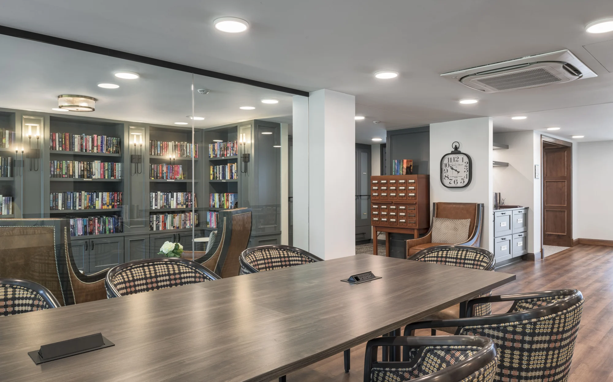 A modern conference room with a large meeting table, surrounded by stylish chairs and bookshelves.