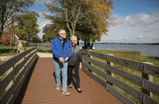 An elderly couple enjoys a pleasant walk along the lakeside on a sunny autumn day.