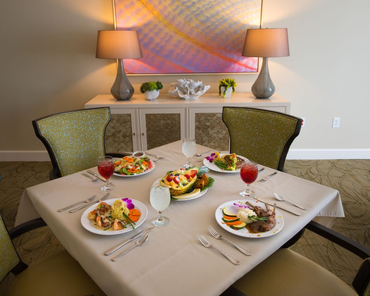 A stylishly set dining table with plates of food and drinks, surrounded by elegant chairs and illuminated by warm lamps.