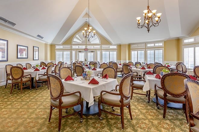 An elegantly set dining room with multiple tables and chairs, featuring chandeliers and a bright, inviting interior.
