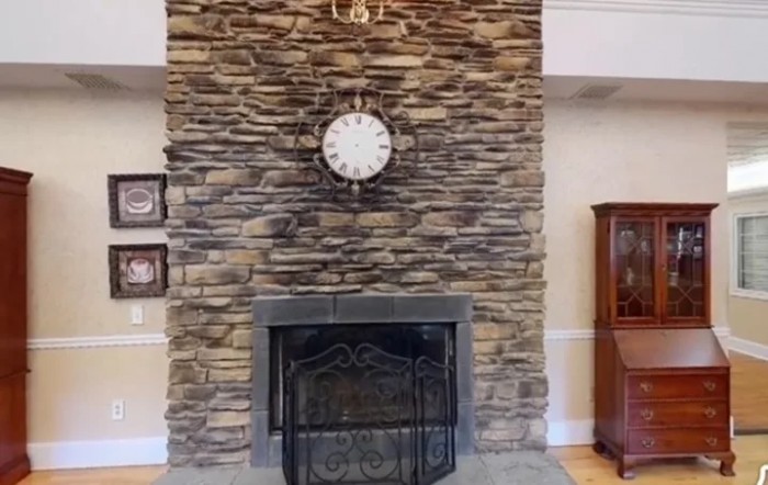 A traditional stone fireplace with a decorative clock mounted above, showcasing classic home decor.