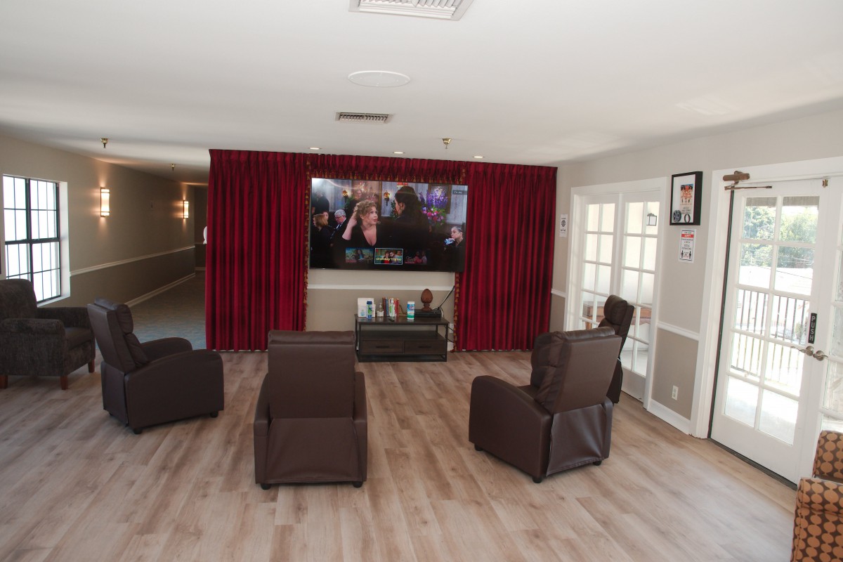 A cozy home theater setup with comfortable recliners facing a large television, enhanced by red curtains and a wooden floor.