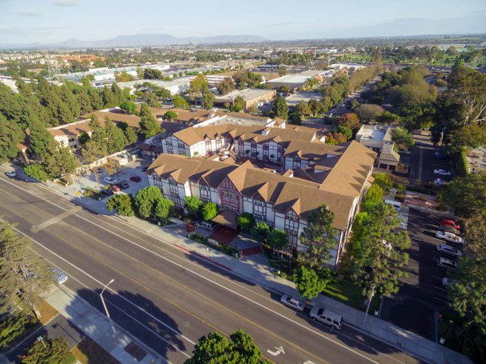 Aerial view of a suburban residential area with a prominent road and surrounding trees.