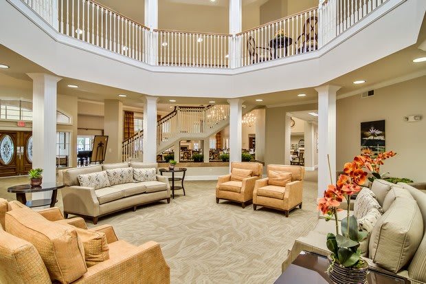 A spacious lobby featuring elegant furniture, a grand staircase, and decorative columns.