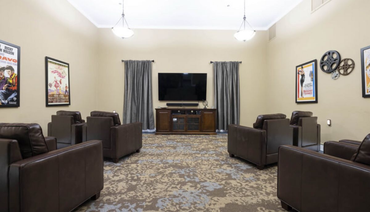 A cozy living room setup with multiple comfortable chairs, a large television, and curtains framing the windows.