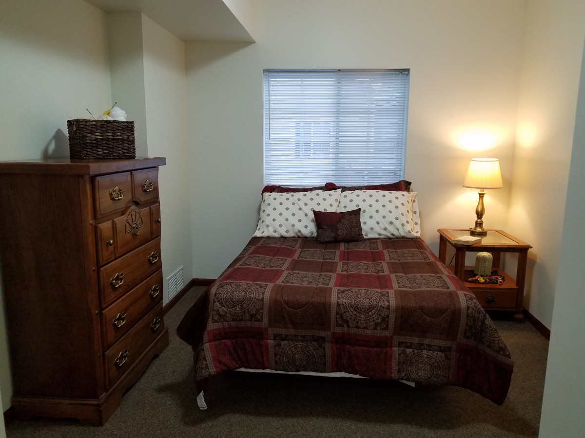 Cozy bedroom with a bed, dresser, and lamp.