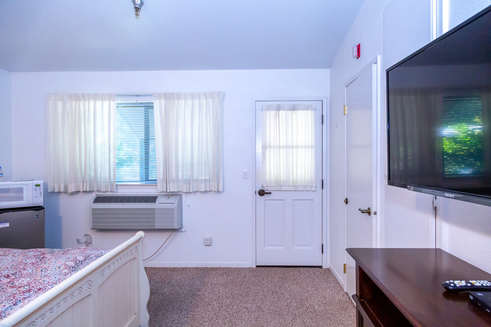 A cozy bedroom featuring a window, air conditioner, and television.