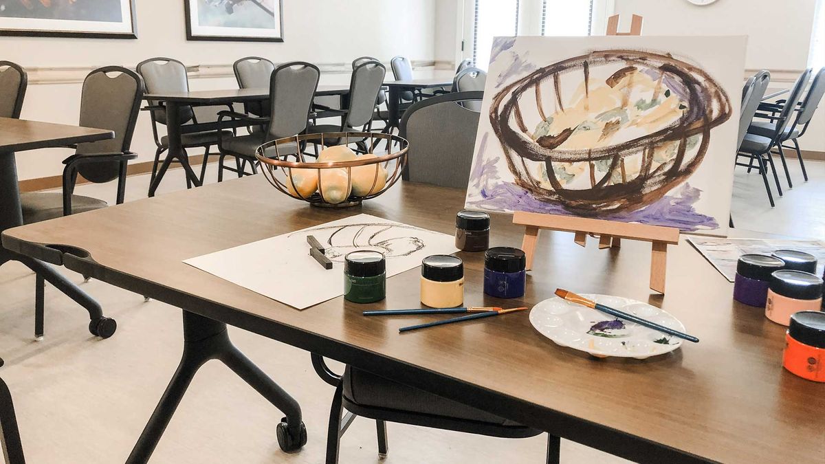 A tabletop setup for a painting session featuring still life art with a bowl of fruit, paints, and brushes.