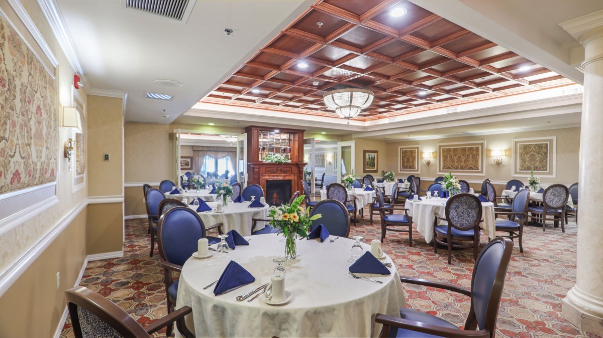 An elegant dining room with round tables set for a formal event, featuring blue chairs and a cozy fireplace.