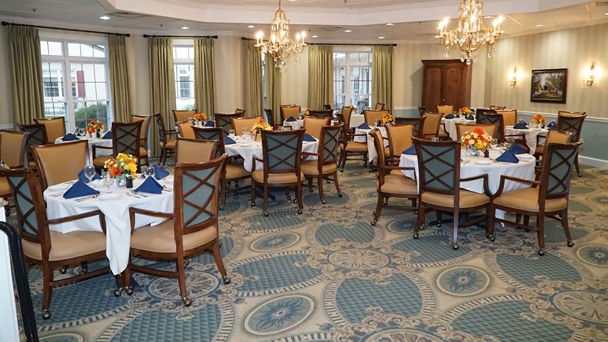 A spacious and elegantly decorated dining room with multiple tables and chairs, featuring chandeliers and a patterned carpet.