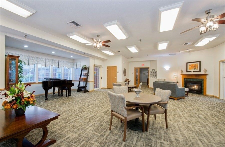 A spacious and well-lit living area featuring comfortable seating, tables, and a grand piano.