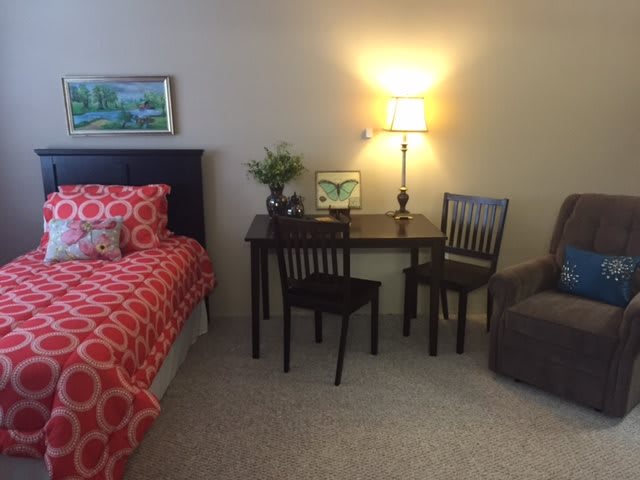 A cozy bedroom with a neatly made bed, a small table with chairs, and a lit lamp for a warm ambiance.