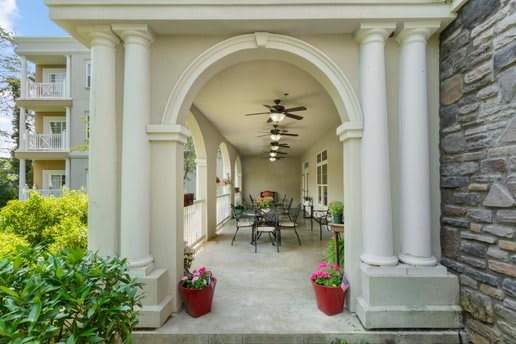 A classic porch with columns and archway, featuring outdoor seating and potted plants.