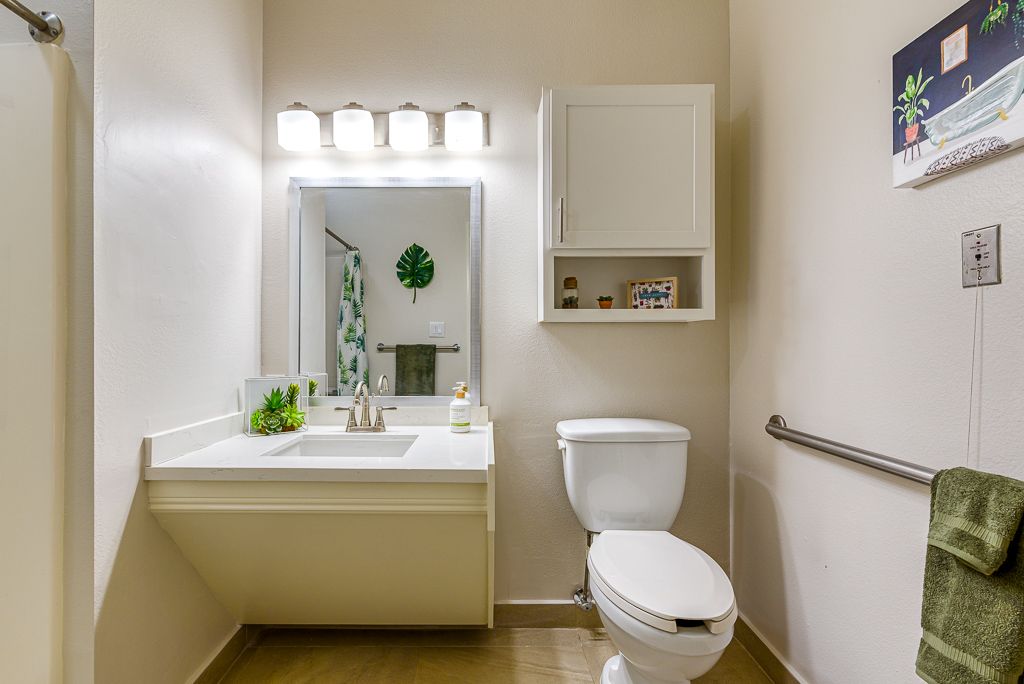 A clean and modern bathroom featuring a sink with a large mirror, toilet, and wall-mounted cabinet.