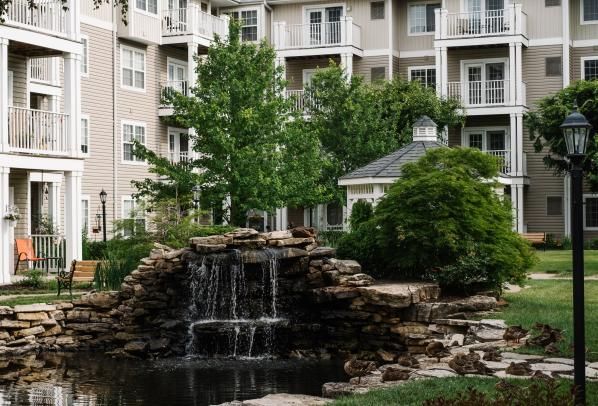 A tranquil waterfall feature in front of an apartment building surrounded by lush greenery.