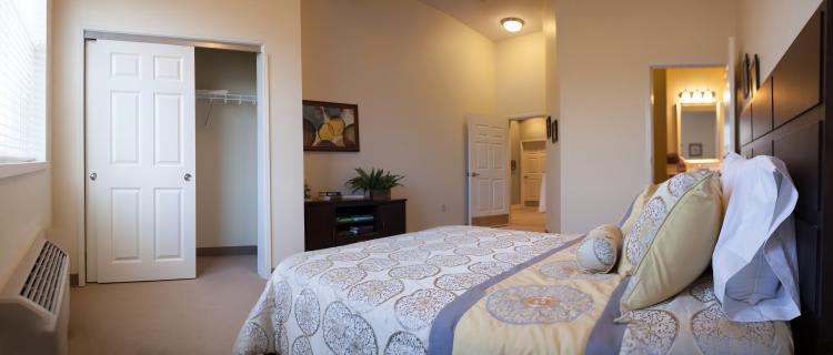 A cozy bedroom with neutral colors, featuring a bed with patterned bedding and a small dresser.