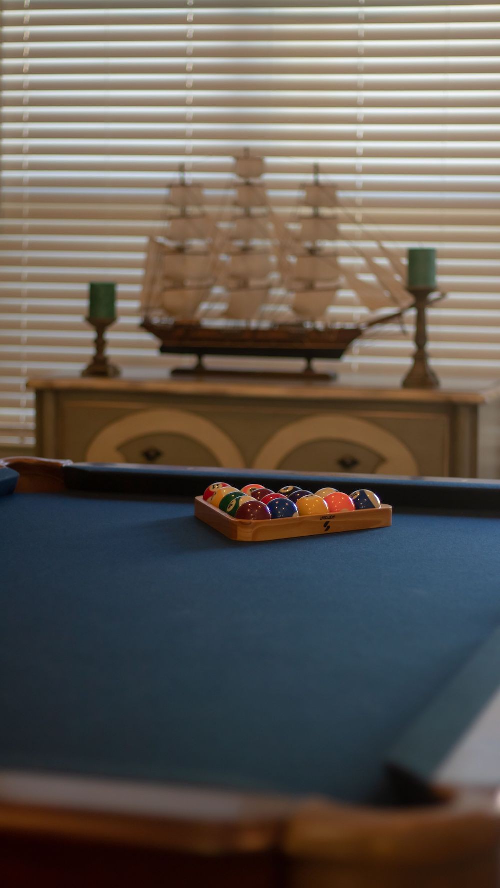 A pool table set with billiard balls, accompanied by candles and a model ship in the background.