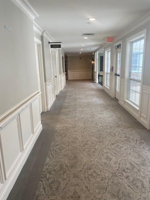 A bright hallway with carpeted floors, lined with doors and windows.