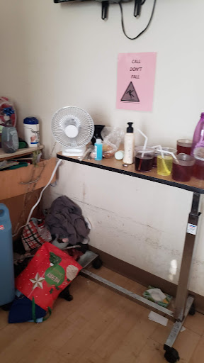 A cluttered workspace filled with various items including bottles, a fan, and some bags.