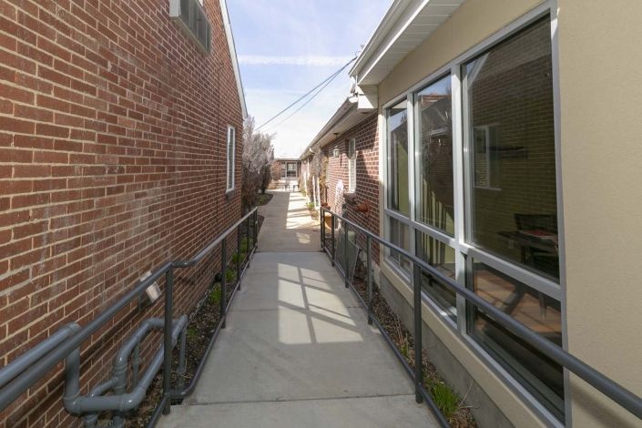 A narrow alleyway with railings leading between two brick and beige buildings.