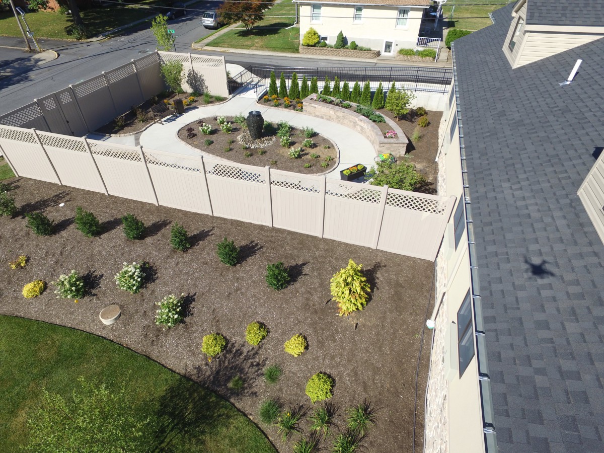Aerial view of a landscaped garden with a pathway and shrubs surrounded by a fence.