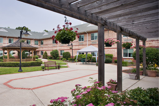 A serene courtyard featuring blooming flowers, hanging plants, and benches, surrounded by a welcoming building.