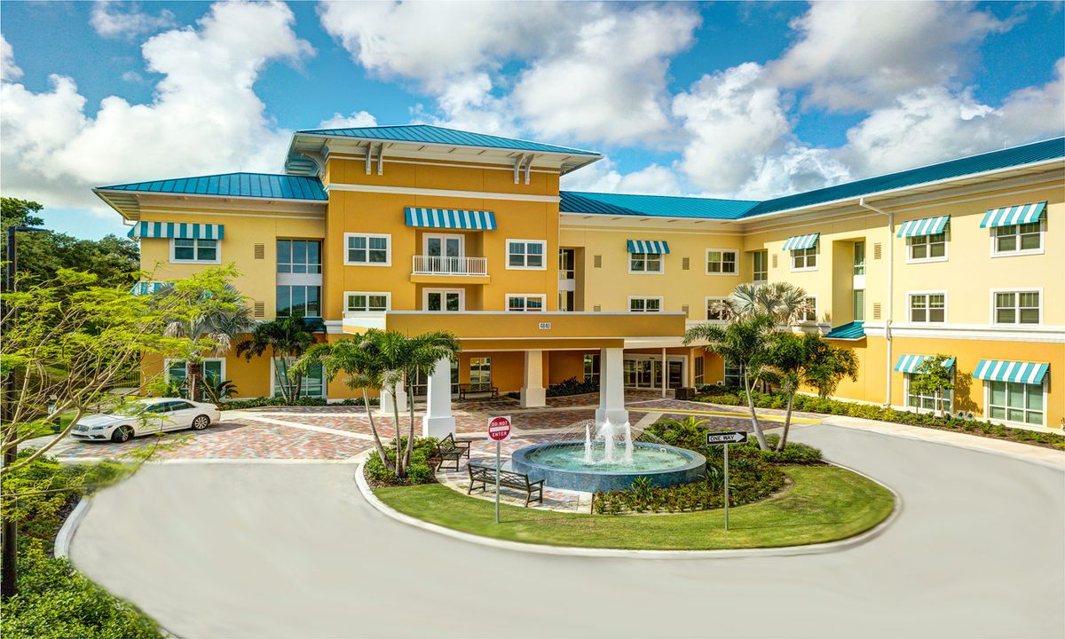 A bright yellow residential building with a fountain in front, surrounded by trees and a clear blue sky.