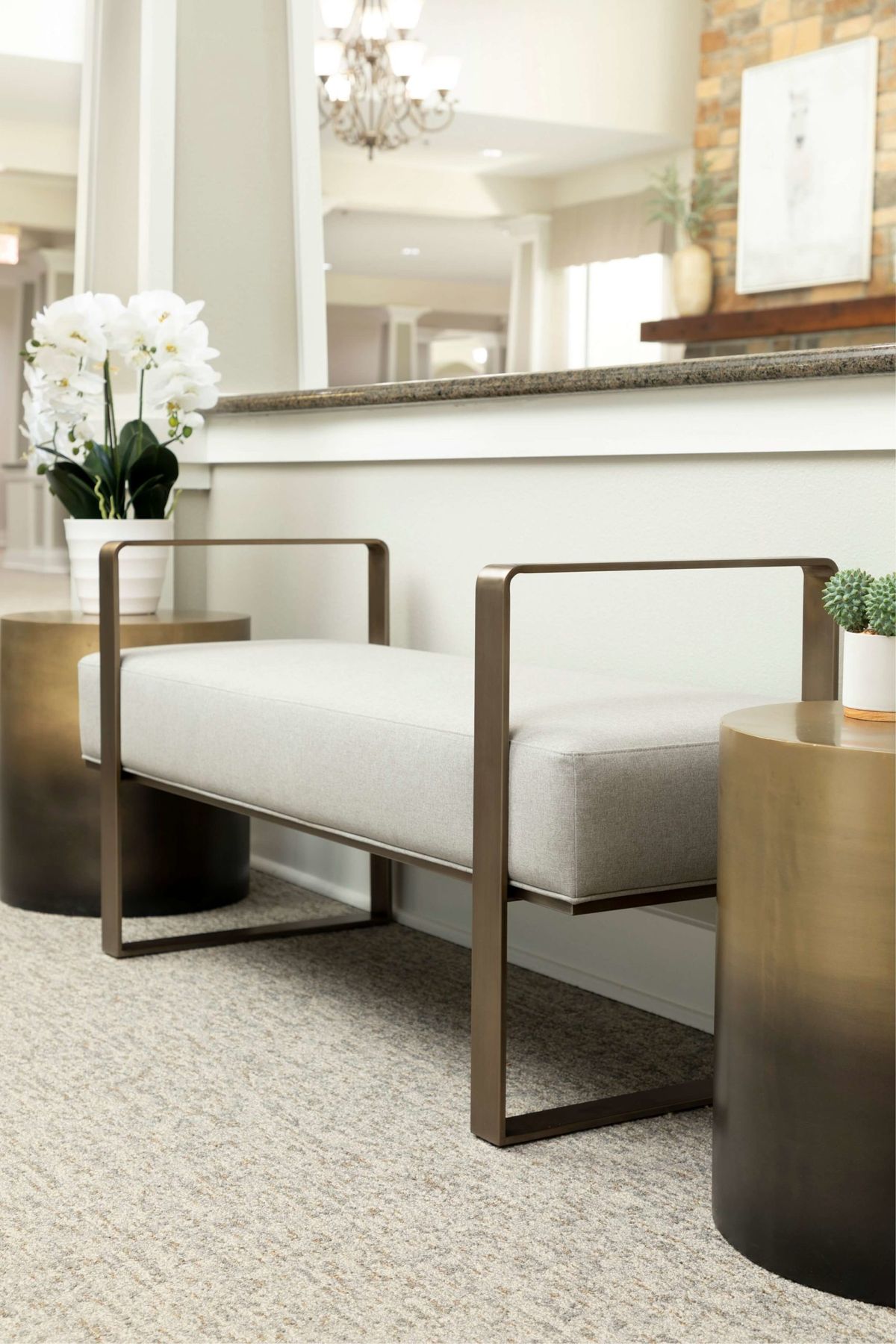 A modern and minimalist bench with sleek metal arms, accompanied by side tables and a white orchid in an elegant interior setting.