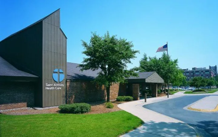 Exterior view of a health care clinic with surrounding trees and an American flag in the background.