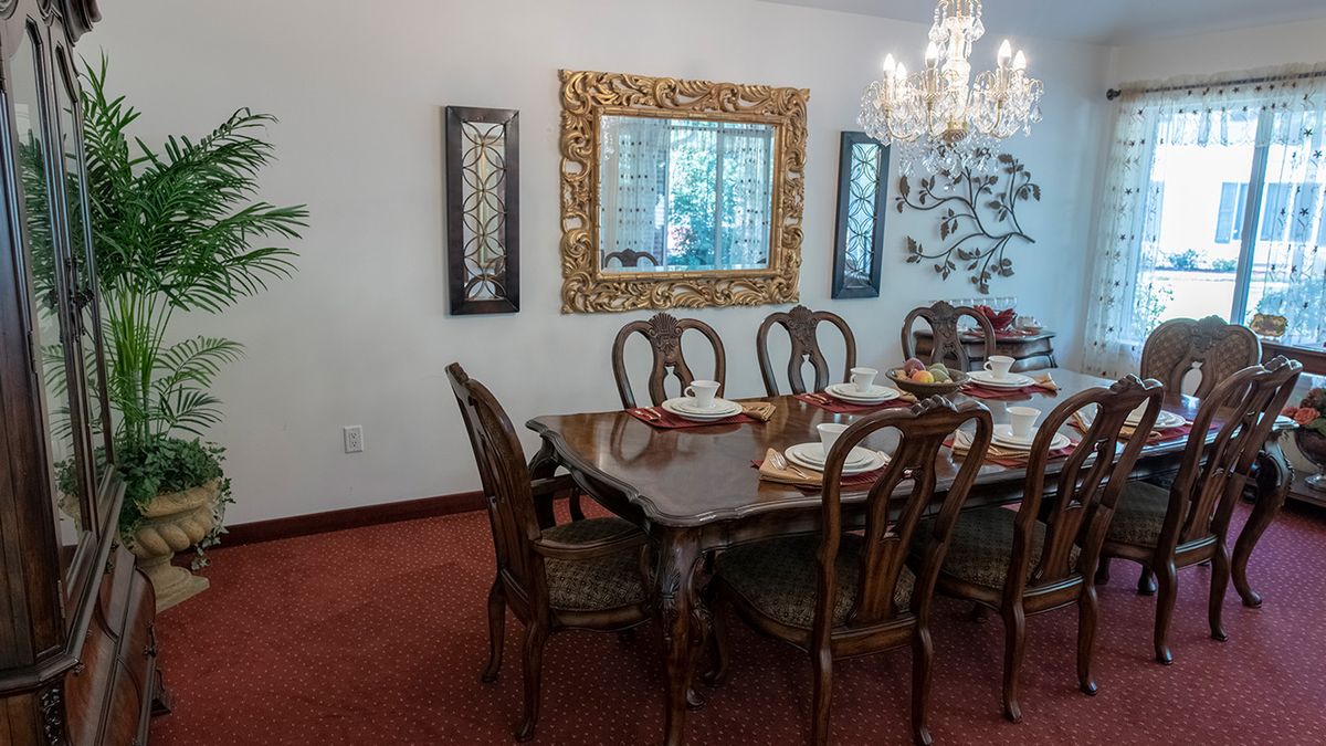Elegant dining room with a wooden table and chairs, adorned by a chandelier and decorative mirror.