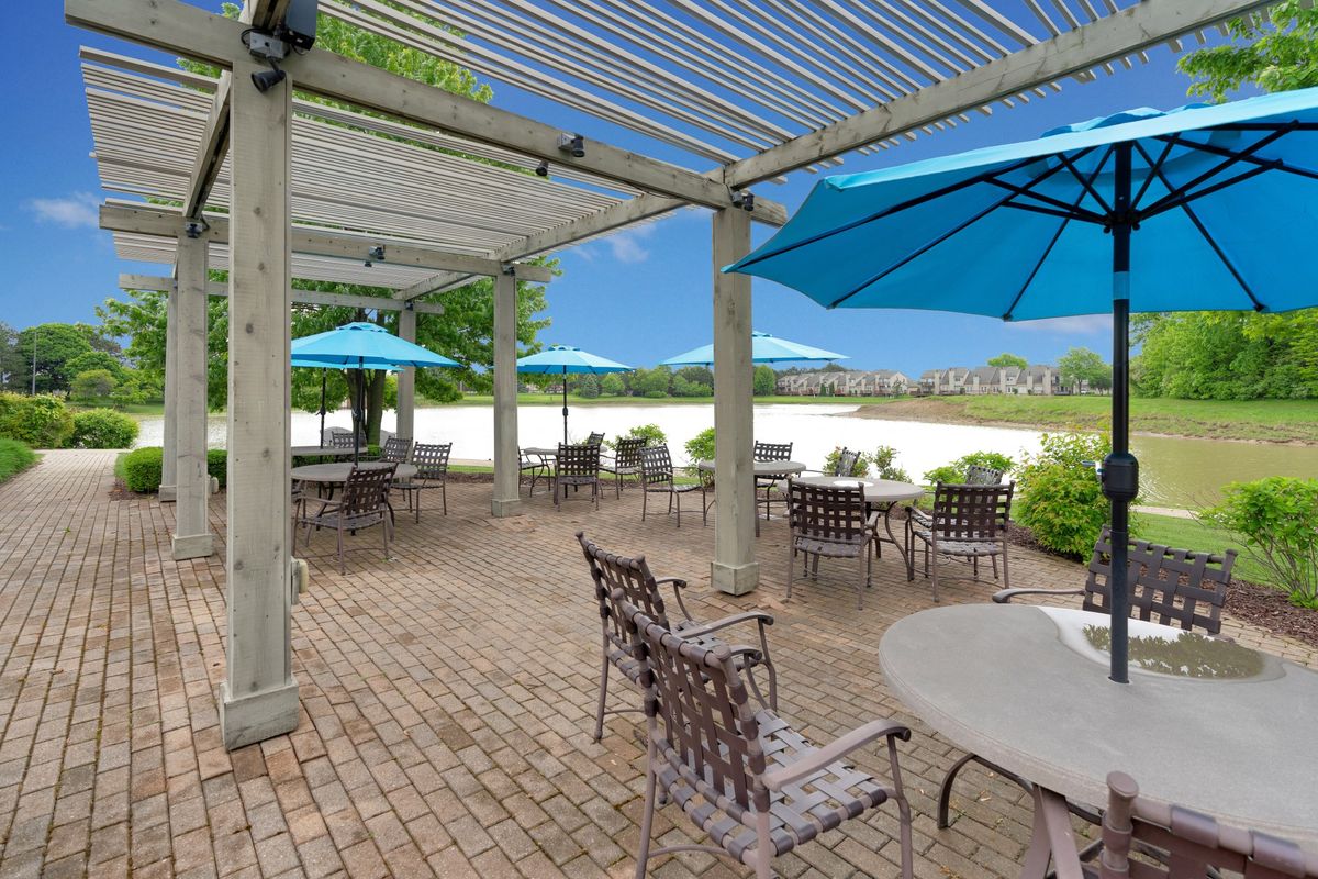 A tranquil outdoor patio with tables and chairs under a pergola and blue umbrellas.