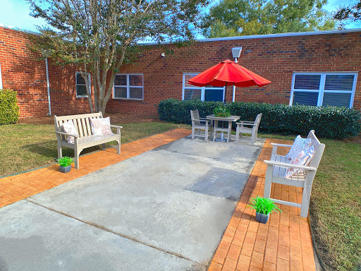 A serene outdoor patio area featuring comfortable benches, a dining table with a red umbrella, and well-maintained landscaping.