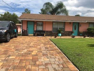A suburban house with a brick driveway and lush lawn under a cloudy sky.