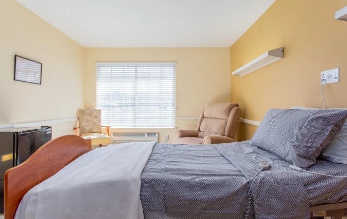 A minimalist bedroom with a large bed, chairs, and a window allowing natural light.