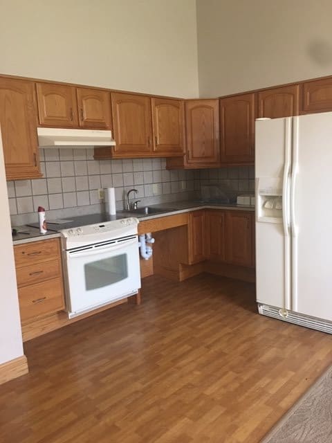 A kitchen featuring wooden cabinets, a refrigerator, and a stove with wood flooring.