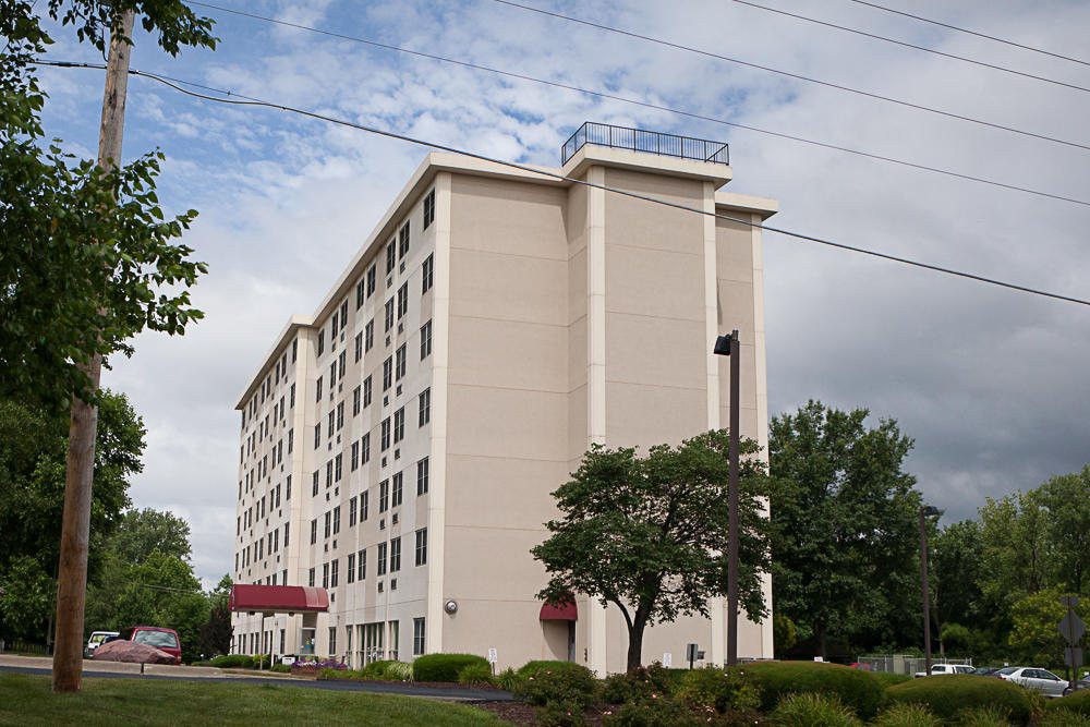 A multi-story hotel building with trees in the foreground under a partly cloudy sky.