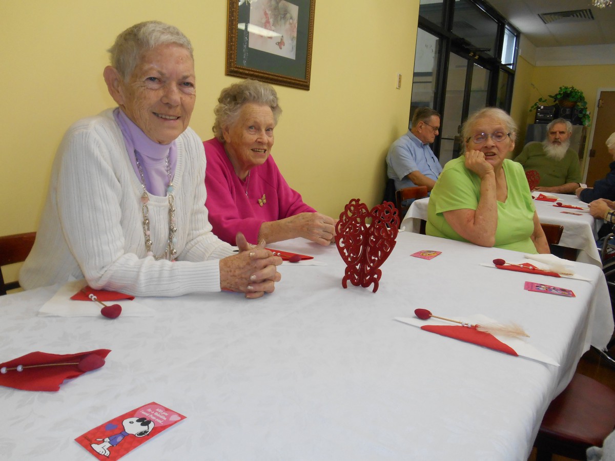 A group of elderly women sitting at a decorated table during an indoor gathering.