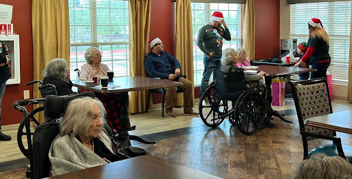 Seniors enjoying a holiday gathering in their activity room, wearing festive red hats.