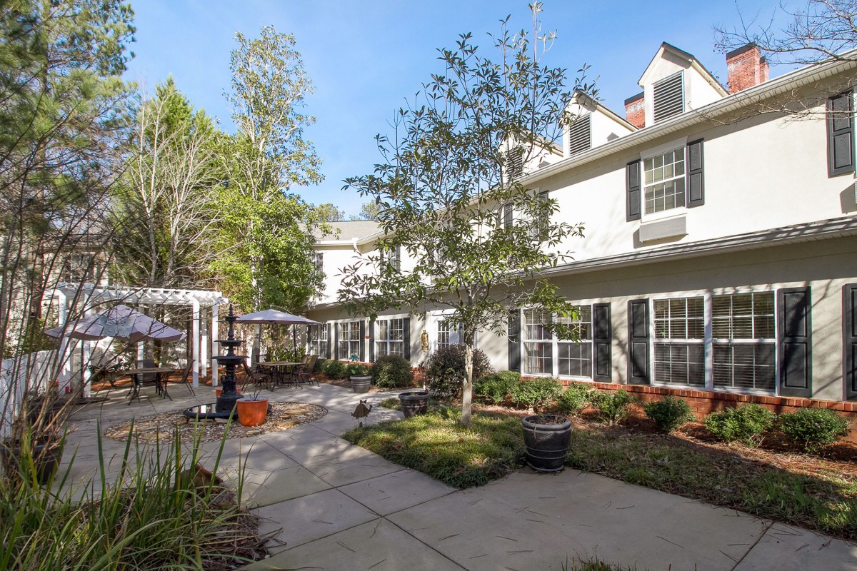 A serene courtyard with greenery and a two-story building in the background on a sunny day.